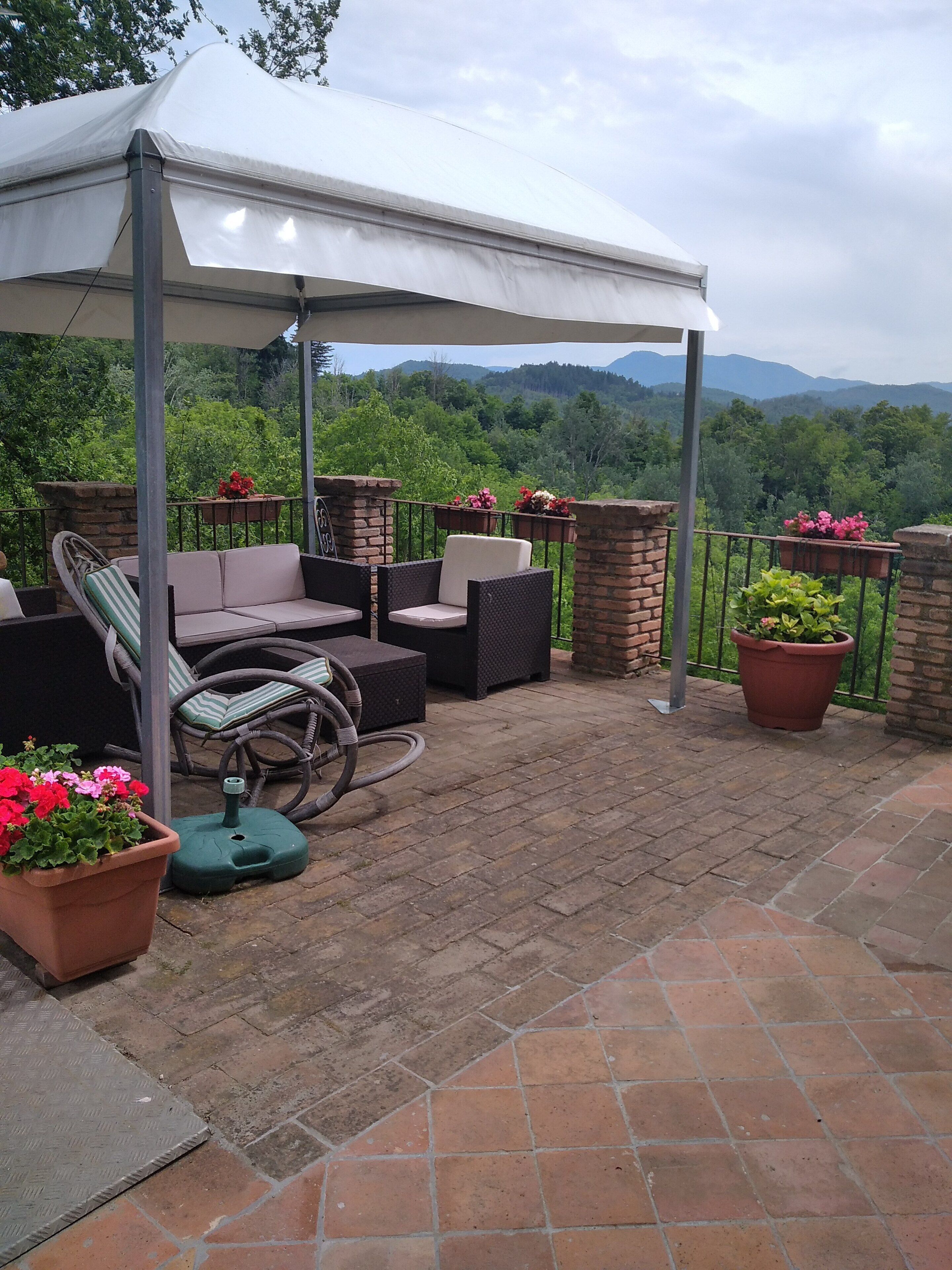 Ein überdachter Patio-Bereich mit Gartenmöbeln, Topfpflanzen und Blick auf eine gebirgige Landschaft.
