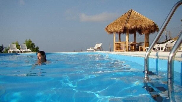 A swimming pool with clear blue water, lounge chairs, and a thatched-roof hut.