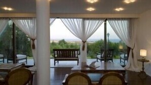 A room with a view of the outdoors, featuring a bench and chairs near the windows.