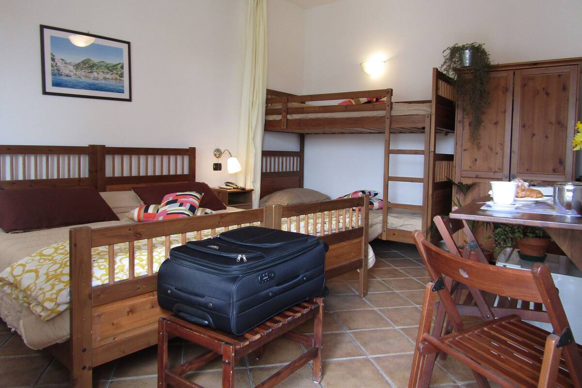 A room with bunk beds, a desk with a chair, a suitcase, and a framed picture on the wall.