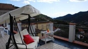 A balcony with a swing chair, a small table, and a white umbrella. - Puesta de Sol (Tramonti)