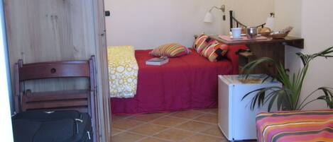 A small, cozy room with a bed, a desk, a chair, and a suitcase.