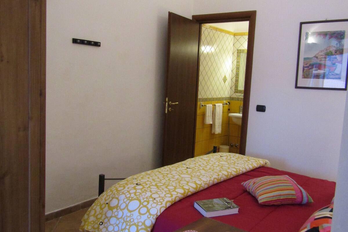 A small, cozy room with a bed, a table with breakfast items, and a mirror reflecting a bathroom.
