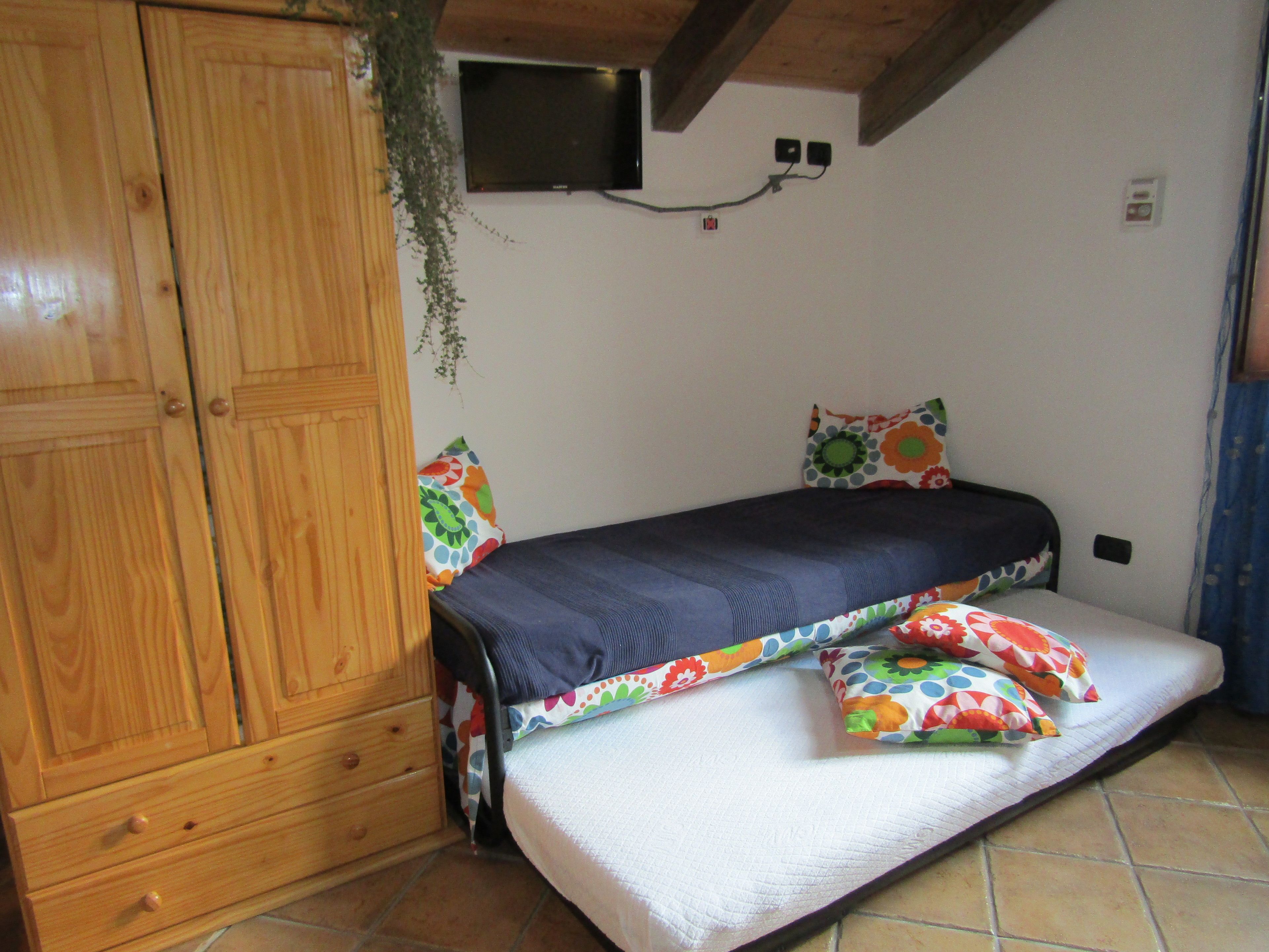 A bedroom with a bed, wooden wardrobe, and a television mounted on the wall.