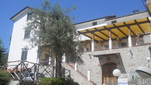 A two-story building with a stone facade, a wooden door, and a yellow awning over the upper floor balcony. - Puesta de Sol (Tramonti)