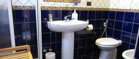 Un baño con un lavamanos blanco, dos inodoros, un espejo y un banco de madera.