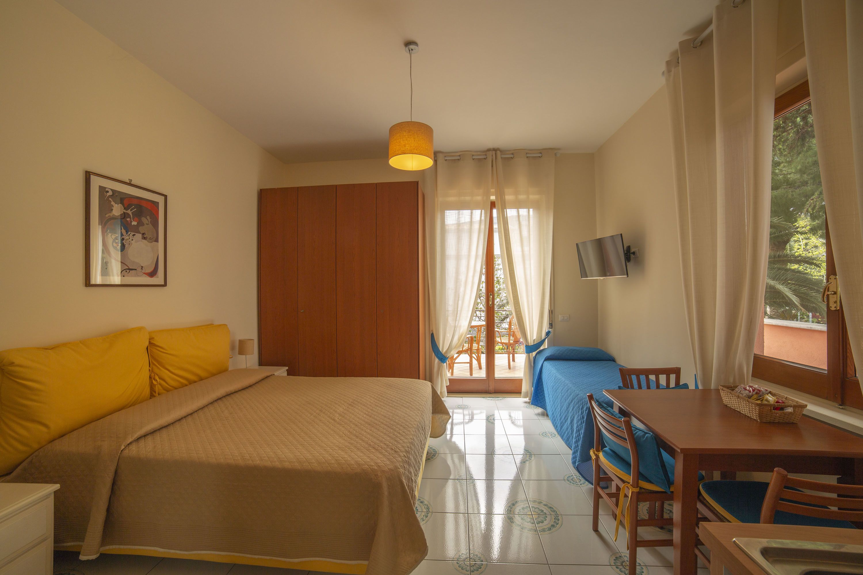 A bedroom with a bed, a desk, a chair, a television, and a window with curtains.
