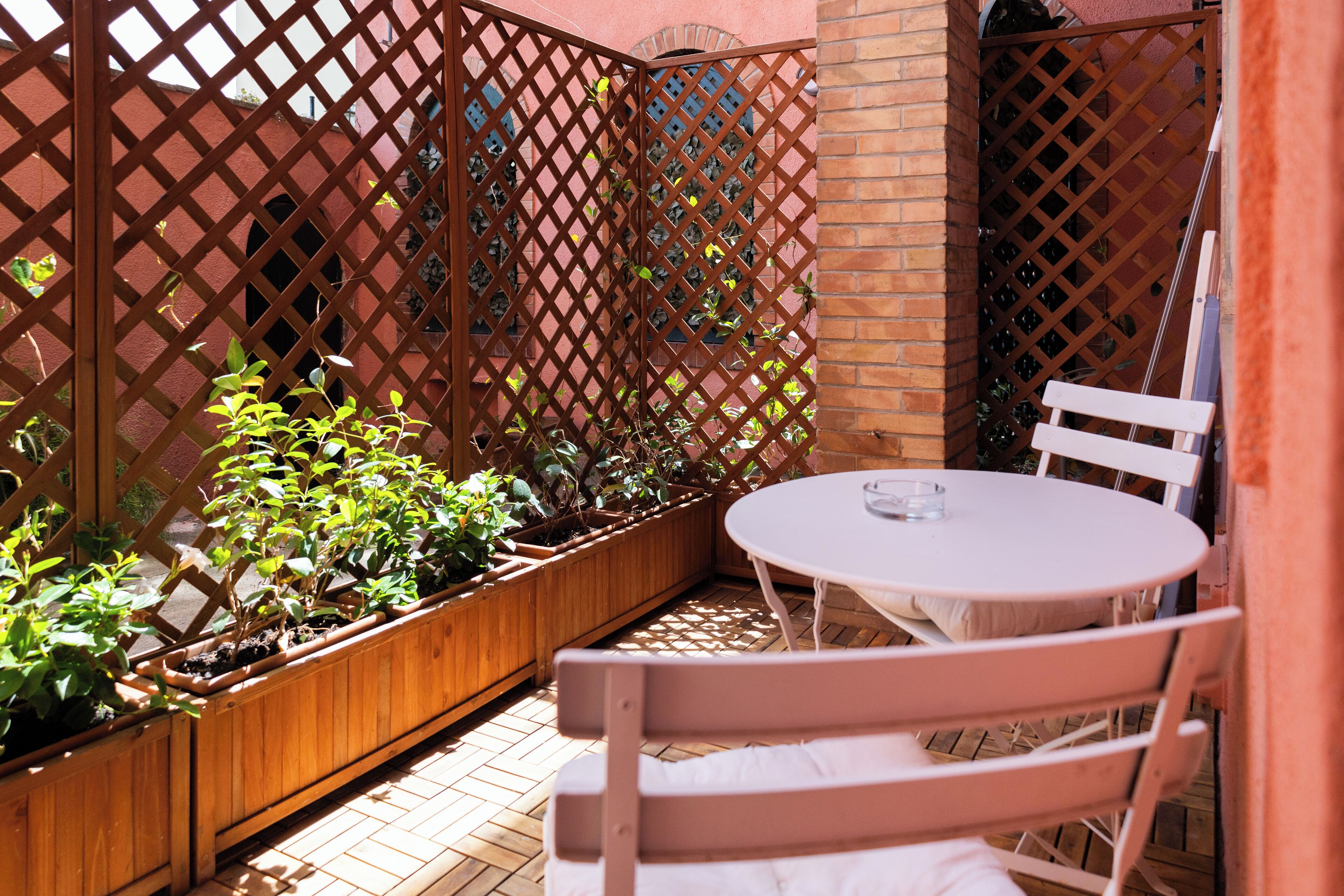 A patio with a round table and chairs, wooden planters with plants, and a lattice fence.