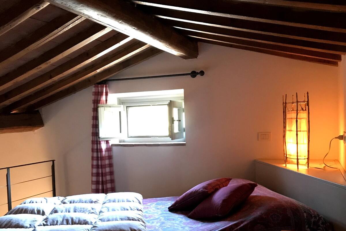 Un dormitorio con cama, ventana con cortinas, lámpara y techo de madera.