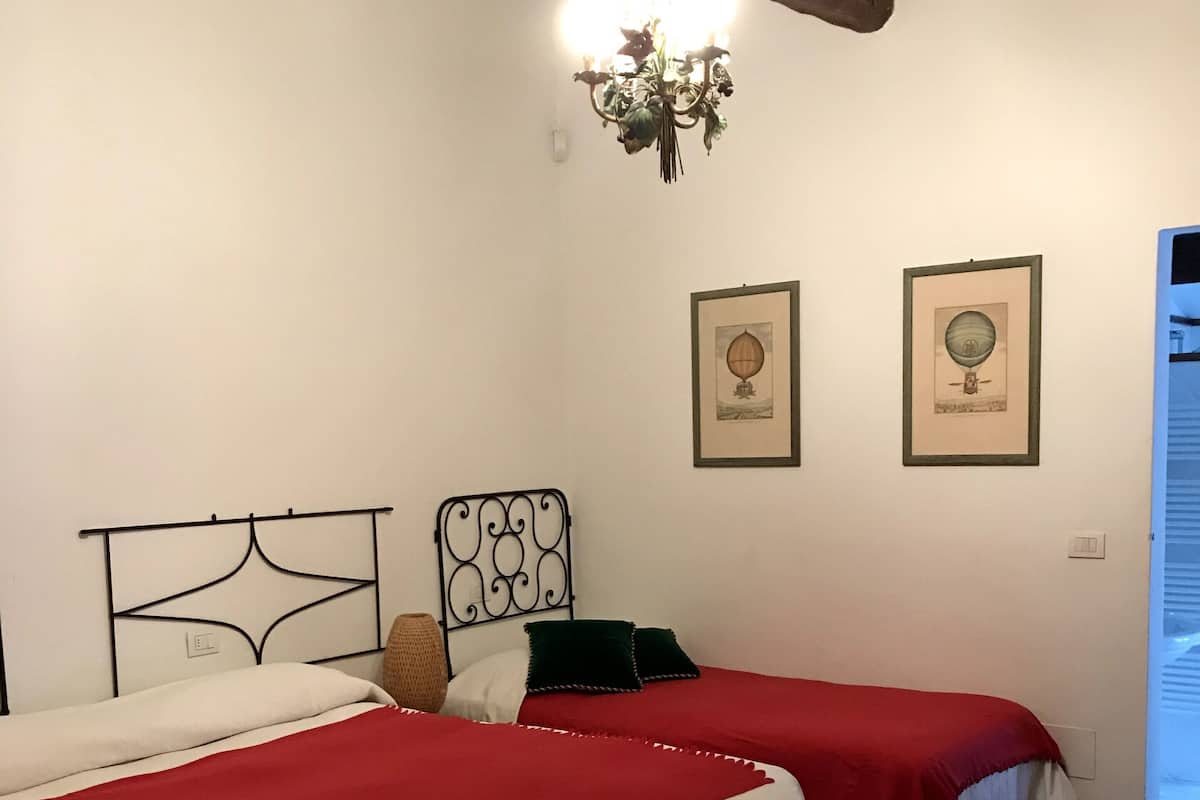 Una habitación con dos camas, cada una con una colcha roja y blanca, techo de madera y dos cuadros enmarcados en la pared.