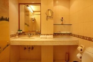 A bathroom with a sink, mirror, towel dispenser, and toilet.