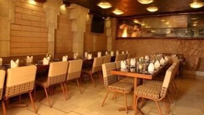 A restaurant with a long wooden table set for a meal, surrounded by wicker chairs. - Hotel Alka Classic (New Delhi)