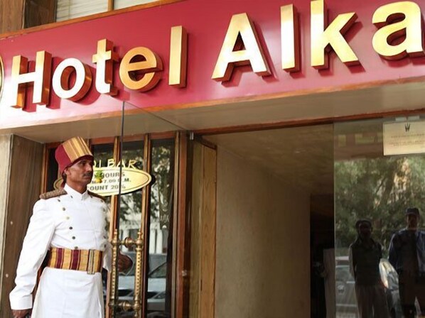 A hotel entrance with a sign reading "Hotel Alka" and a staff member in uniform standing outside.
