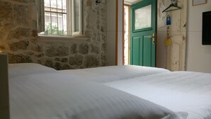 A room with two beds, a stone wall, a green door, and a window with bars. - Apartment Dubrovnik-Center (Dubrovnik)