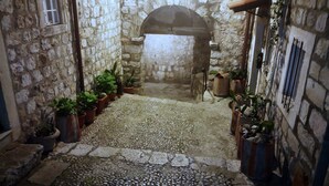 A narrow stone corridor with a cobblestone floor, flanked by potted plants and a rustic stone wall. - Apartment Dubrovnik-Center (Dubrovnik)