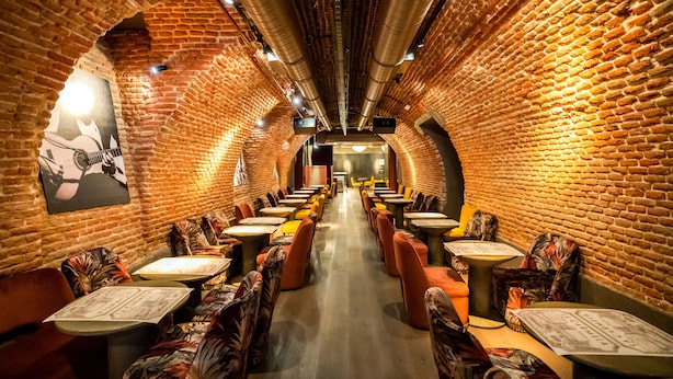 Un restaurant aux murs de briques, avec des tables et des chaises disposées de part et d’autre d’une allée centrale.
