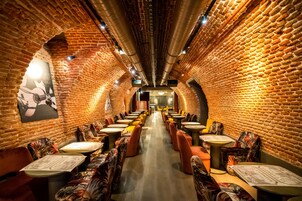 Un ristorante con pareti in mattoni, tavoli e sedie disposti lungo un corridoio centrale.