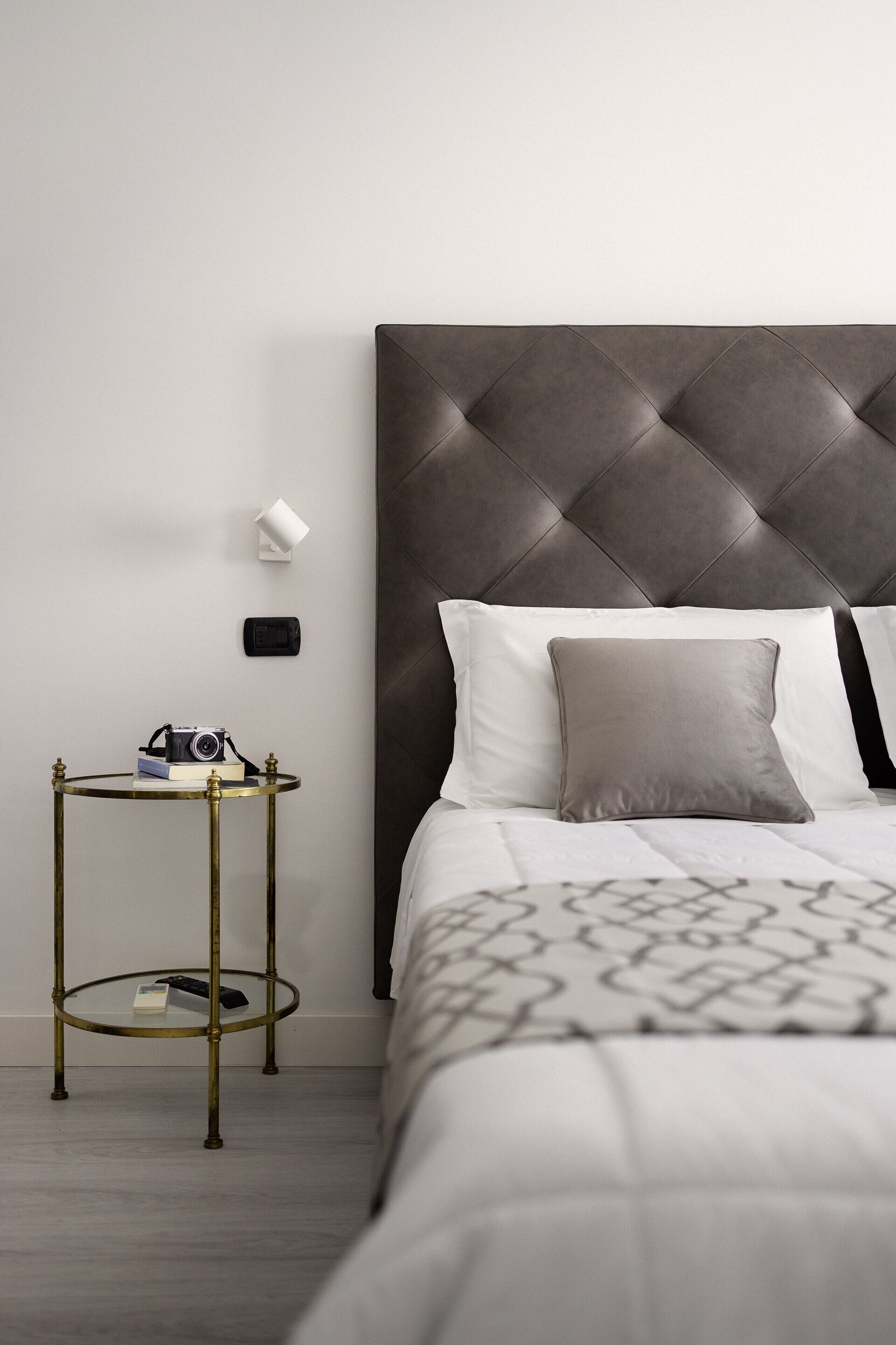 A modern bedroom with a tufted headboard, a round side table with a camera, and a neatly made bed.