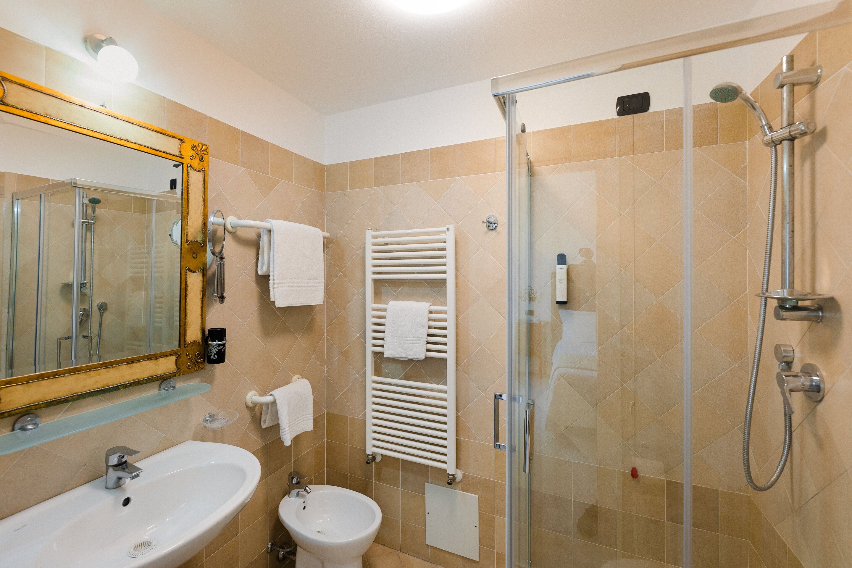 A bathroom with a sink, mirror, towel rack, and a glass-enclosed shower area.