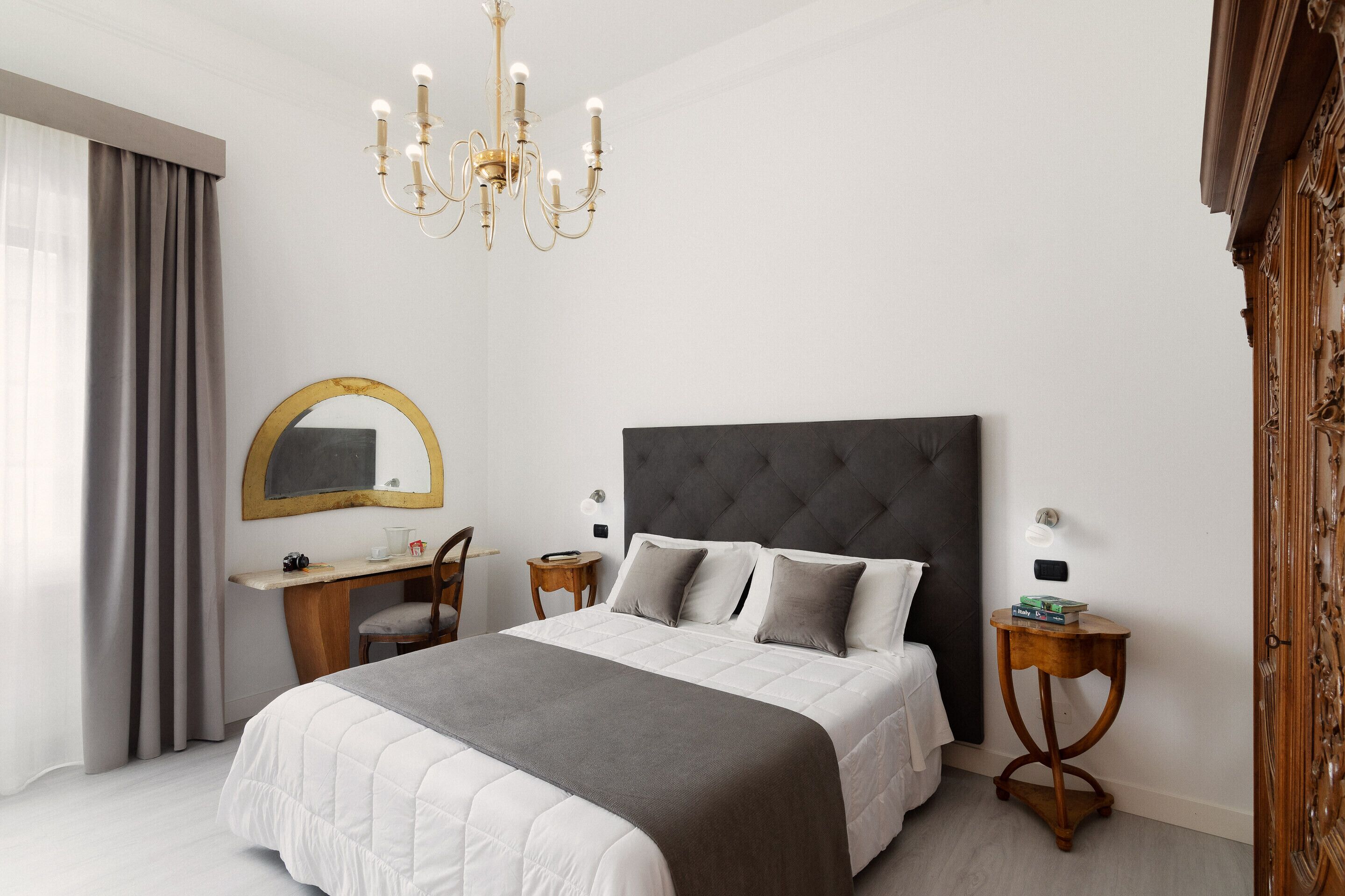 Una camera da letto con un letto grande, una scrivania, una sedia, uno specchio e un lampadario.