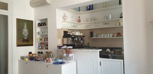 A kitchen with white cabinets, a marble countertop, and shelves with various kitchenware. - Hotel Berna (Florence)