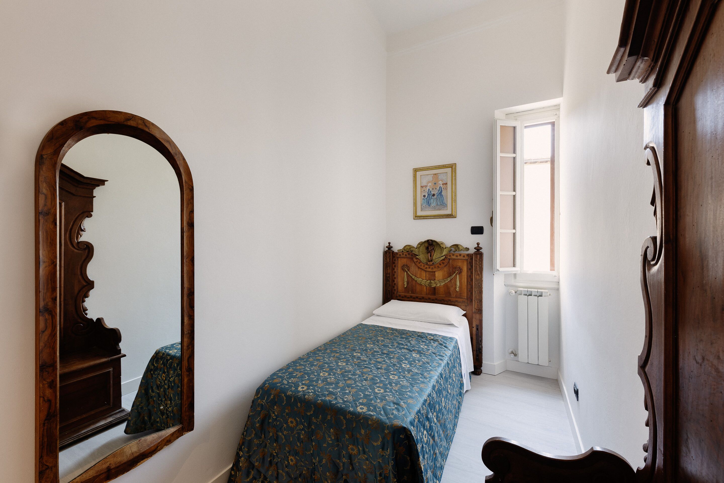 Ein Schlafzimmer mit einem hölzernen Bett, einem großen Spiegel, einem gerahmten Bild an der Wand und einem Fenster mit Heizkörper.