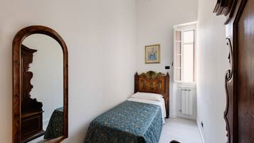 Ein Schlafzimmer mit einem hölzernen Bett, einem großen Spiegel, einem gerahmten Bild an der Wand und einem Fenster mit Heizkörper.