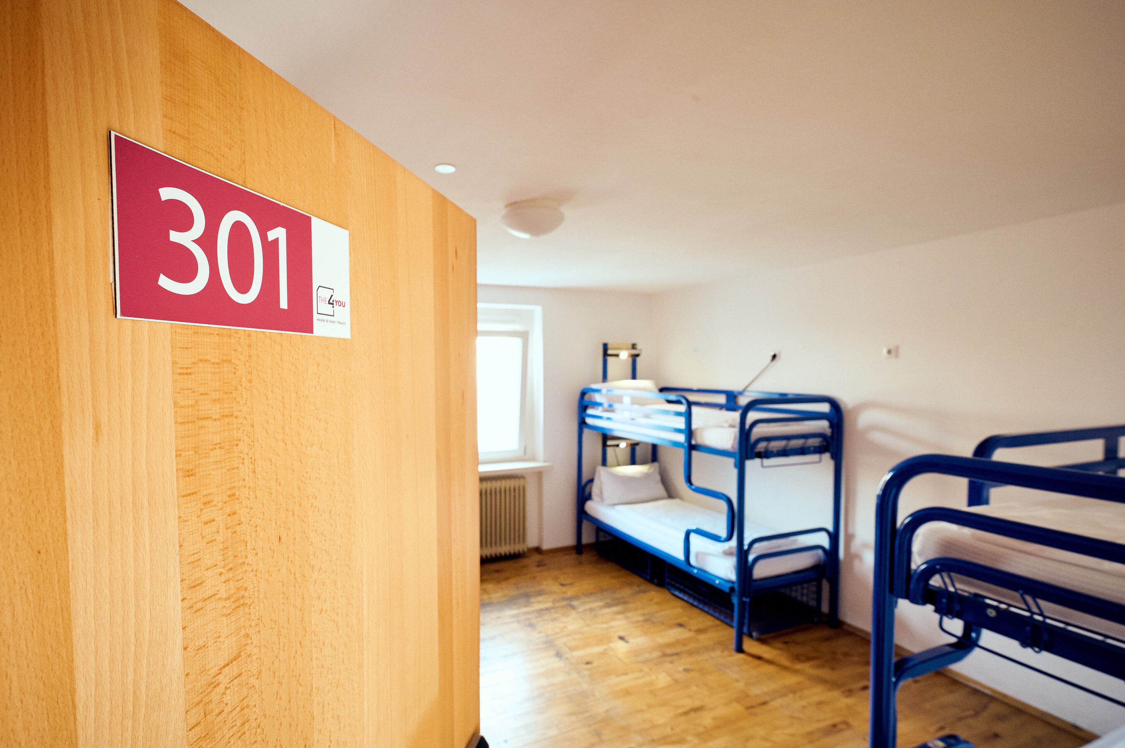 Una habitación con literas, una puerta de madera con un letrero de número y una ventana.