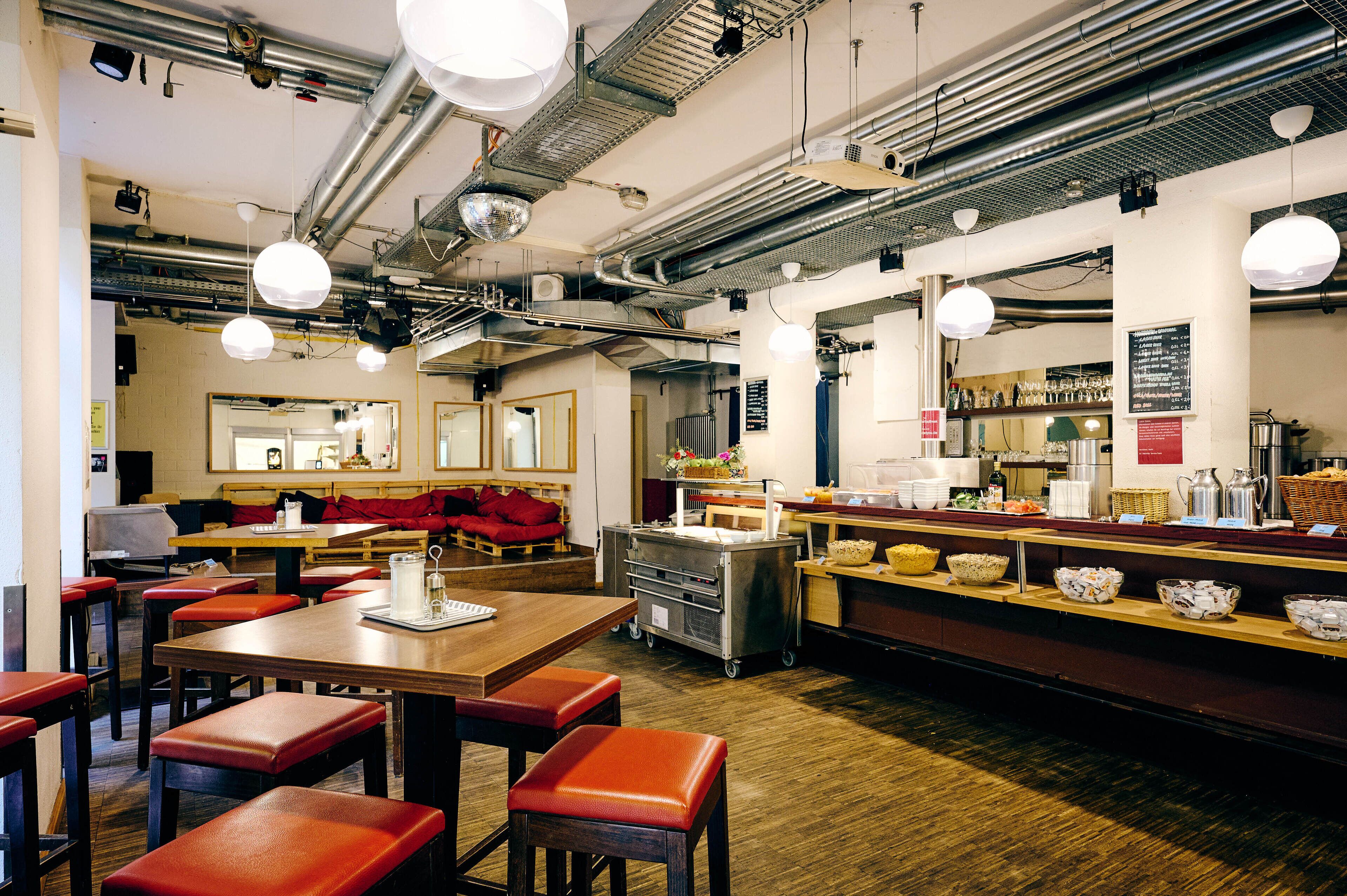 Un restaurant avec des tables en bois et des bancs rembourrés de couleur rouge, un buffet proposant divers plats, et où l’on peut voir l’équipement de la cuisine.