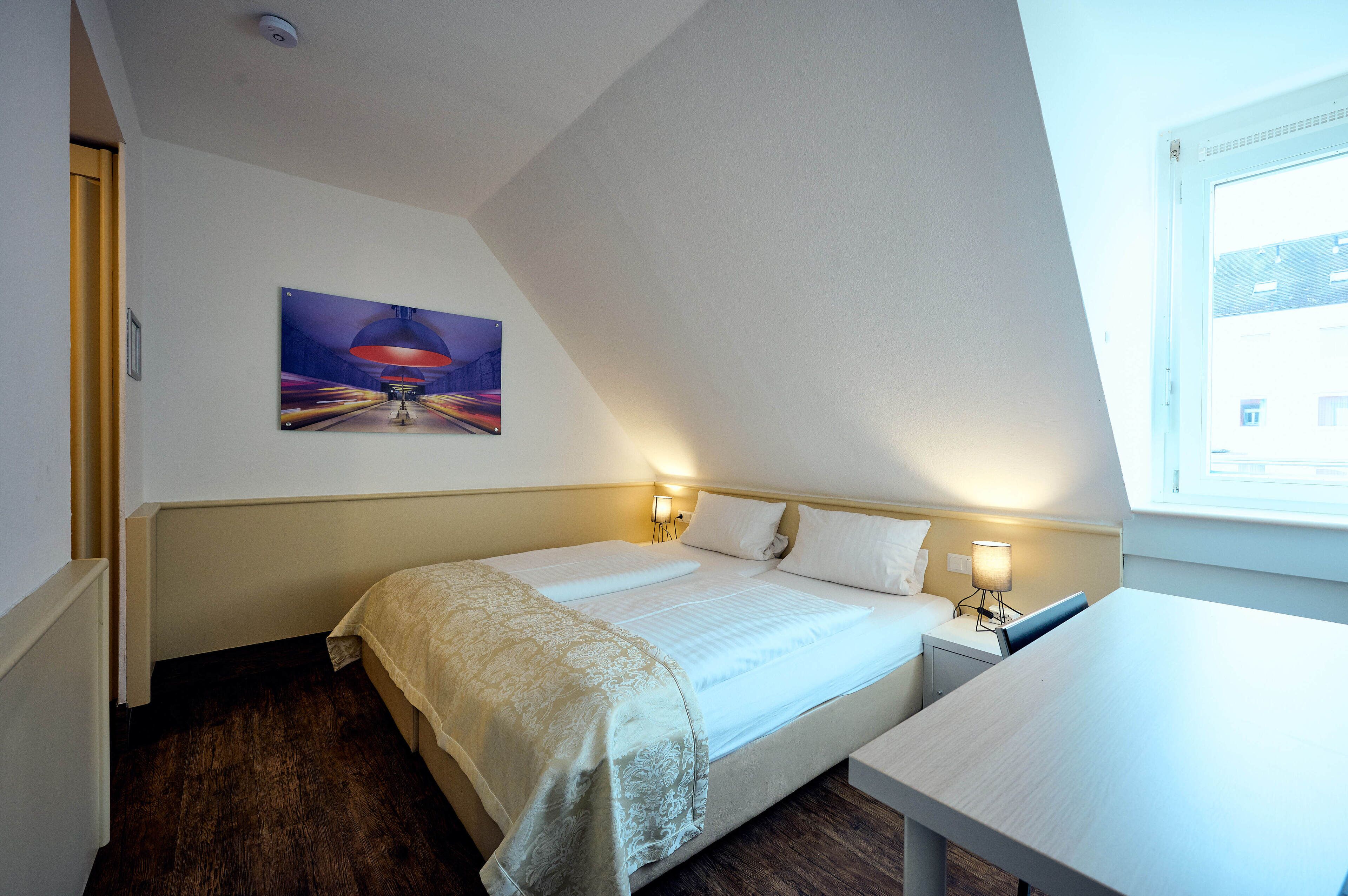 A bedroom with a bed, bedside lamps, a table, and a painting on the wall.