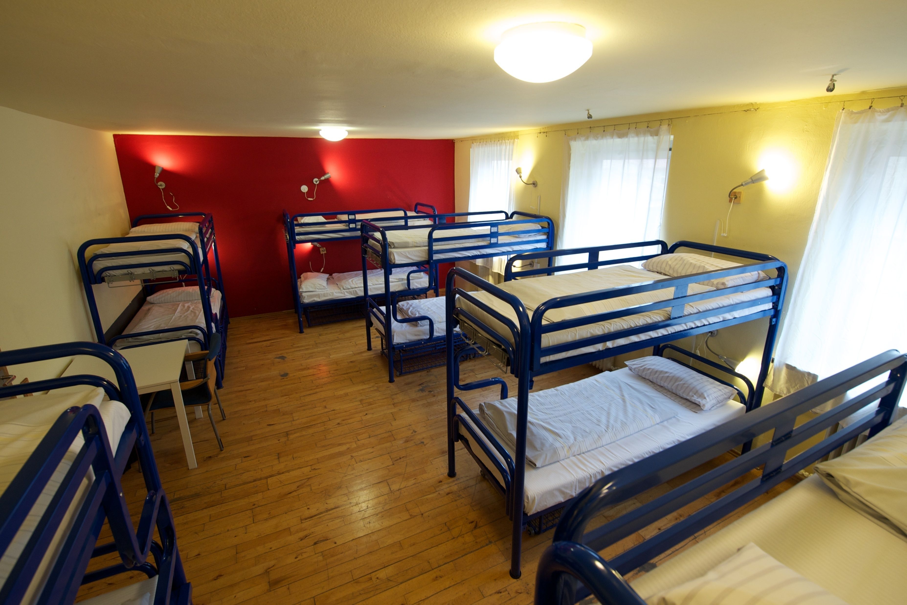 A dormitory room with bunk beds, wooden flooring, and a red accent wall.