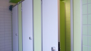 Una hilera de cabinas de baño blancas, con detalles en verde y suelo de baldosas.