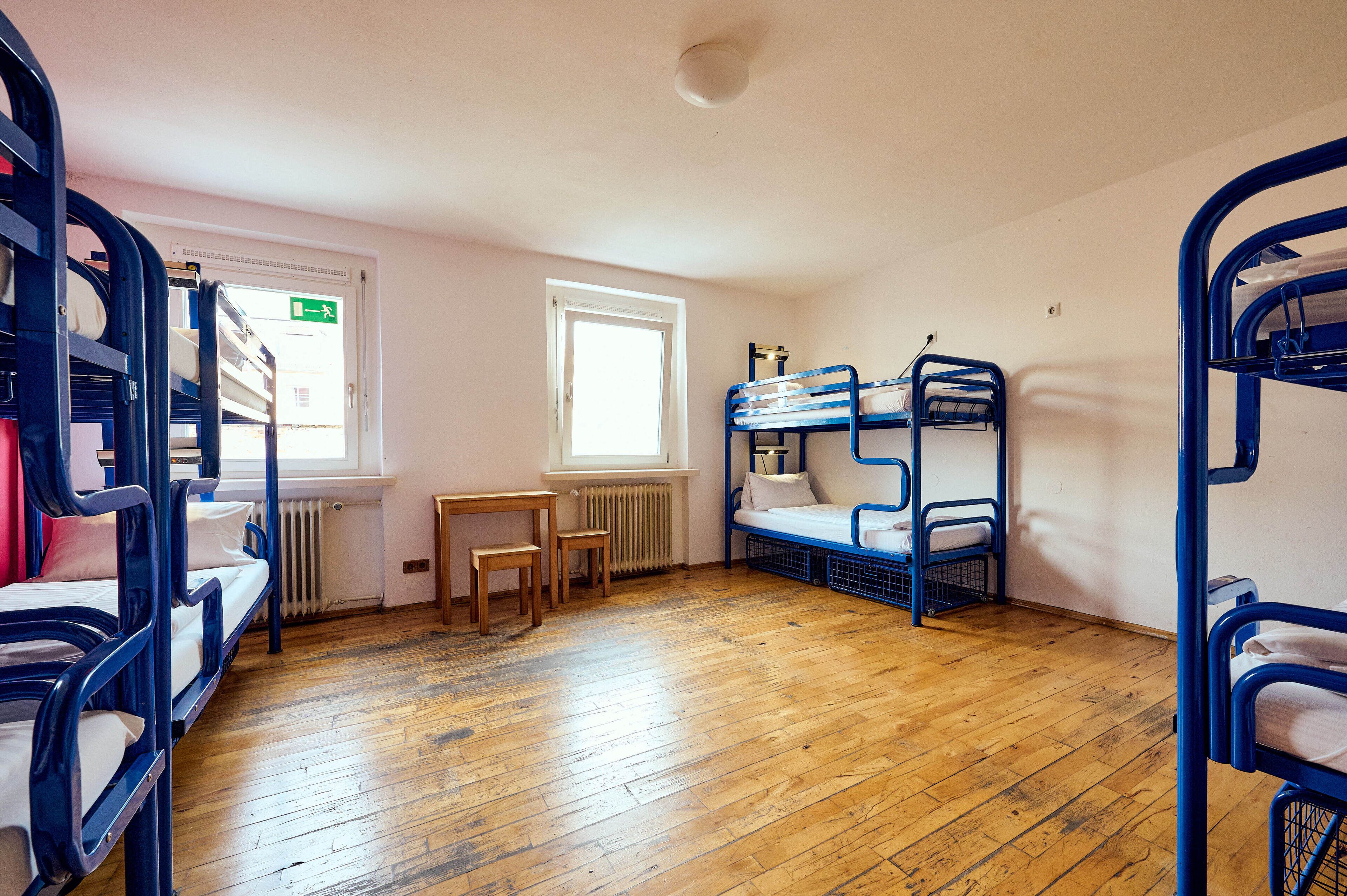 Ein Schlafsaalzimmer mit Etagenbetten, Holzboden, Fenster und Heizkörper.