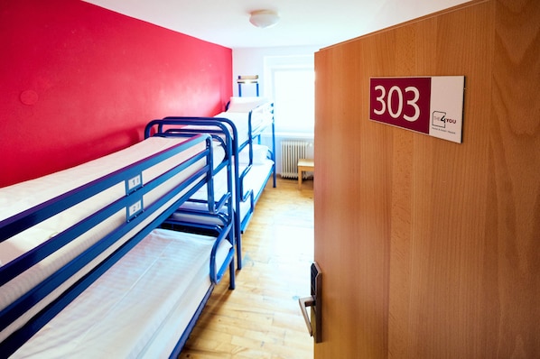 A dormitory room with bunk beds, a wooden door with a number sign, and a radiator in the background. - The 4 You Hostel & Hotel (Munich)