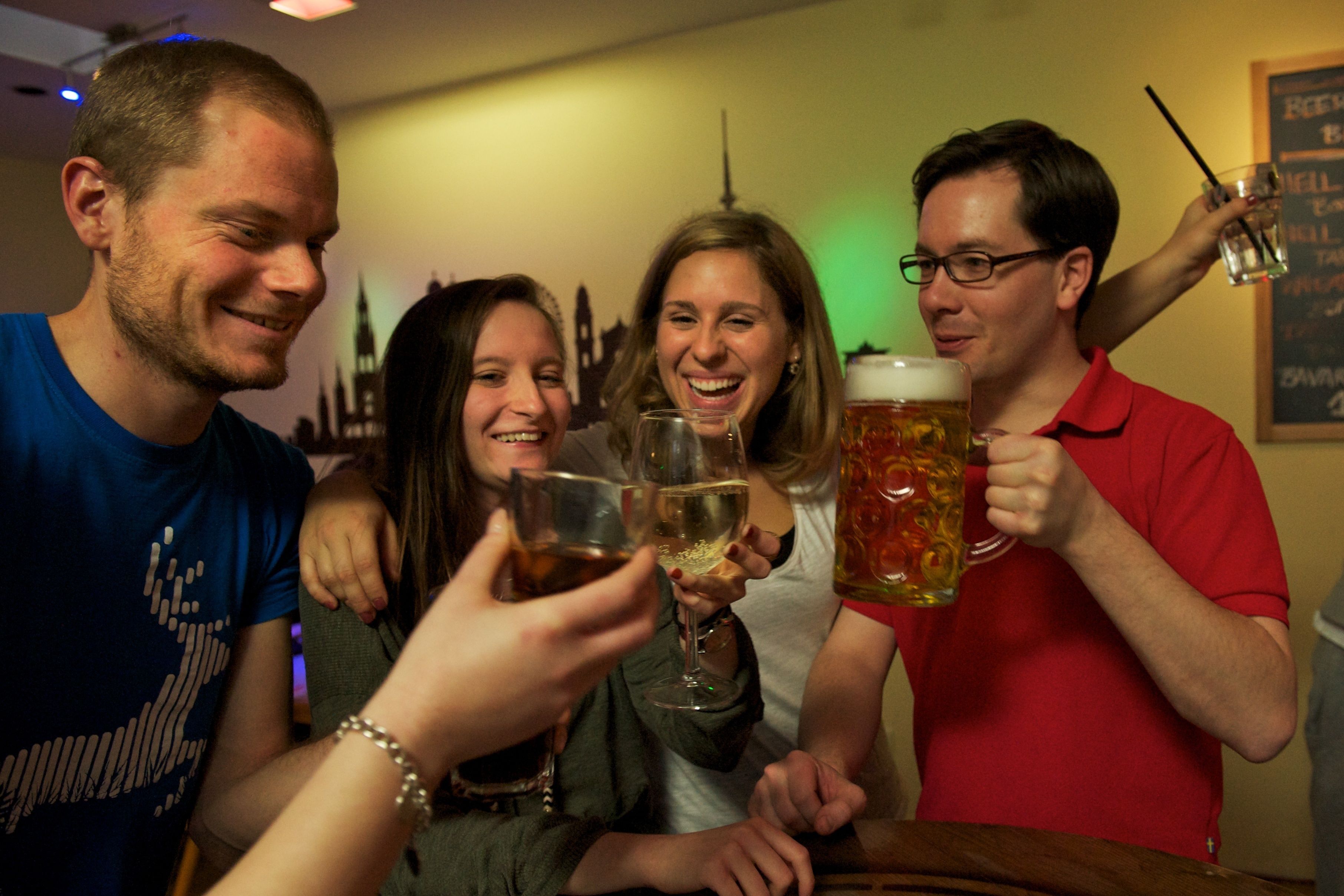 A group of people toasting with drinks in a room with a city skyline mural on the wall.