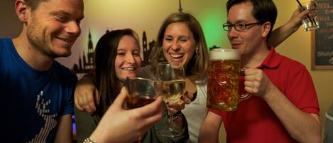 A group of people toasting with drinks in a room with a city skyline mural on the wall.