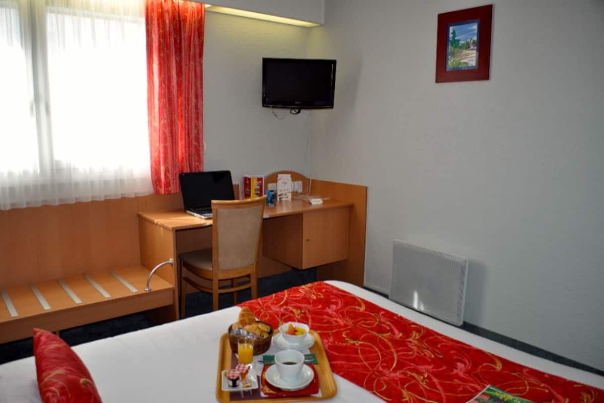 A hotel room with a bed, a desk, a chair, a TV, and a breakfast tray on the bed.
