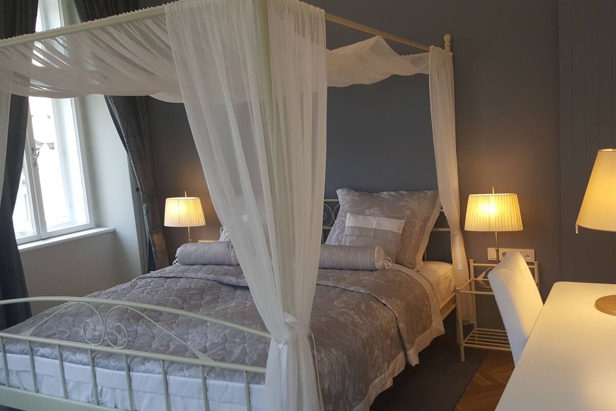 A four-poster bed with a canopy, two bedside lamps, and a bedside table with a lamp.