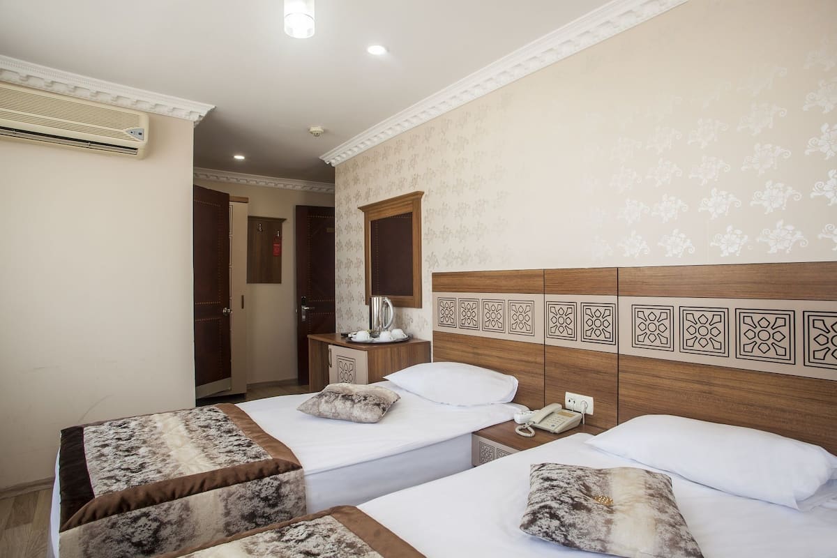 A hotel room with two beds, a wooden headboard, a bedside table with a phone and a kettle, and a mirror above the table.