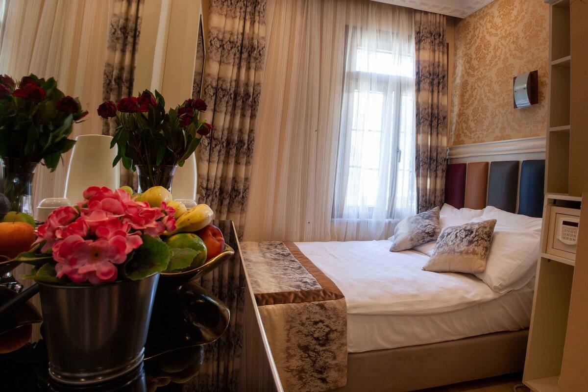 A hotel room with a bed, bedside table, and a window with curtains.