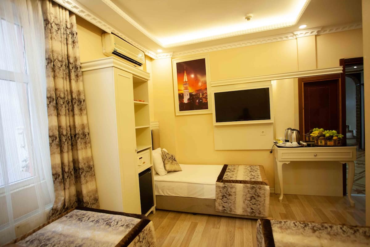 A compact hotel room with a bed, a small desk, a wardrobe, and a wall-mounted TV.