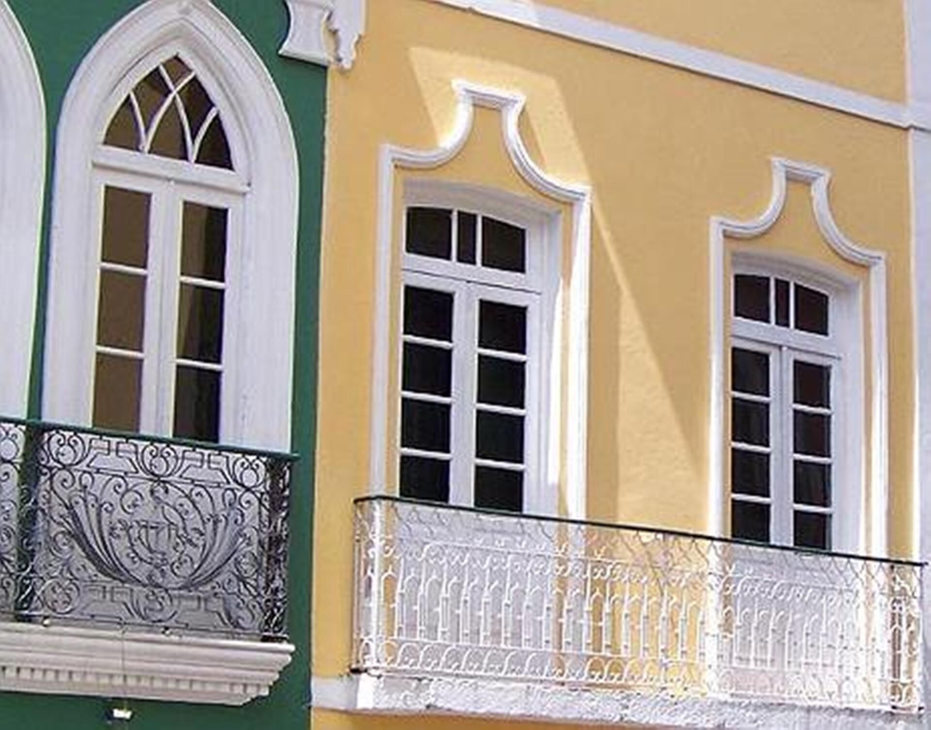 Un edificio con dos ventanas arqueadas de marco blanco y un balcón con barandilla de metal ornamentado.