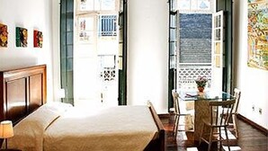 Una habitación con cama, una mesa y sillas. Hay ventanas y una puerta.