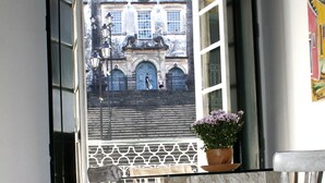 Una habitación con vistas a un edificio histórico a través de una ventana abierta, una silla de madera y una mesita con una planta en maceta.