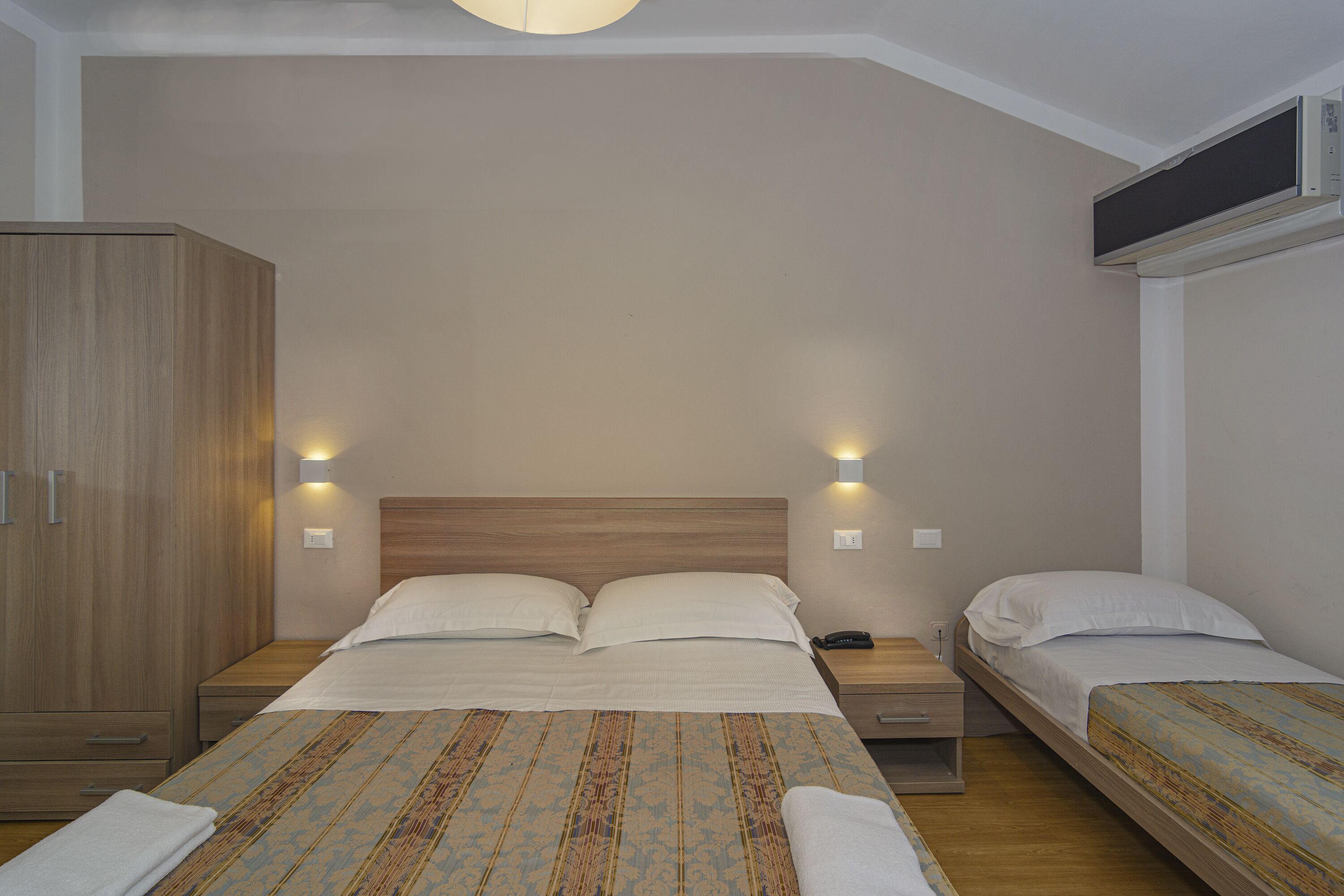 Ein Schlafzimmer mit einem großen Bett, zwei Nachttischen, einem Kleiderschrank und einer Decken-Klimaanlage.