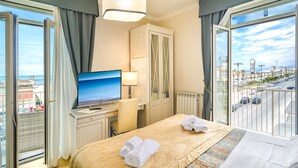 A hotel room with a bed, a TV, a desk, and a view of the city and sea. - Hotel La Pace (Viareggio)