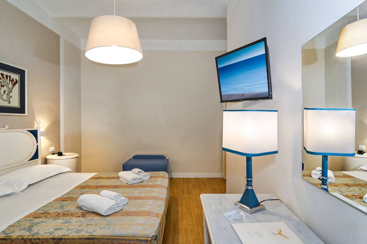 Ein Hotelzimmer mit zwei Betten, einem Fernseher, einem Spiegel und einem Schreibtisch mit Lampe.