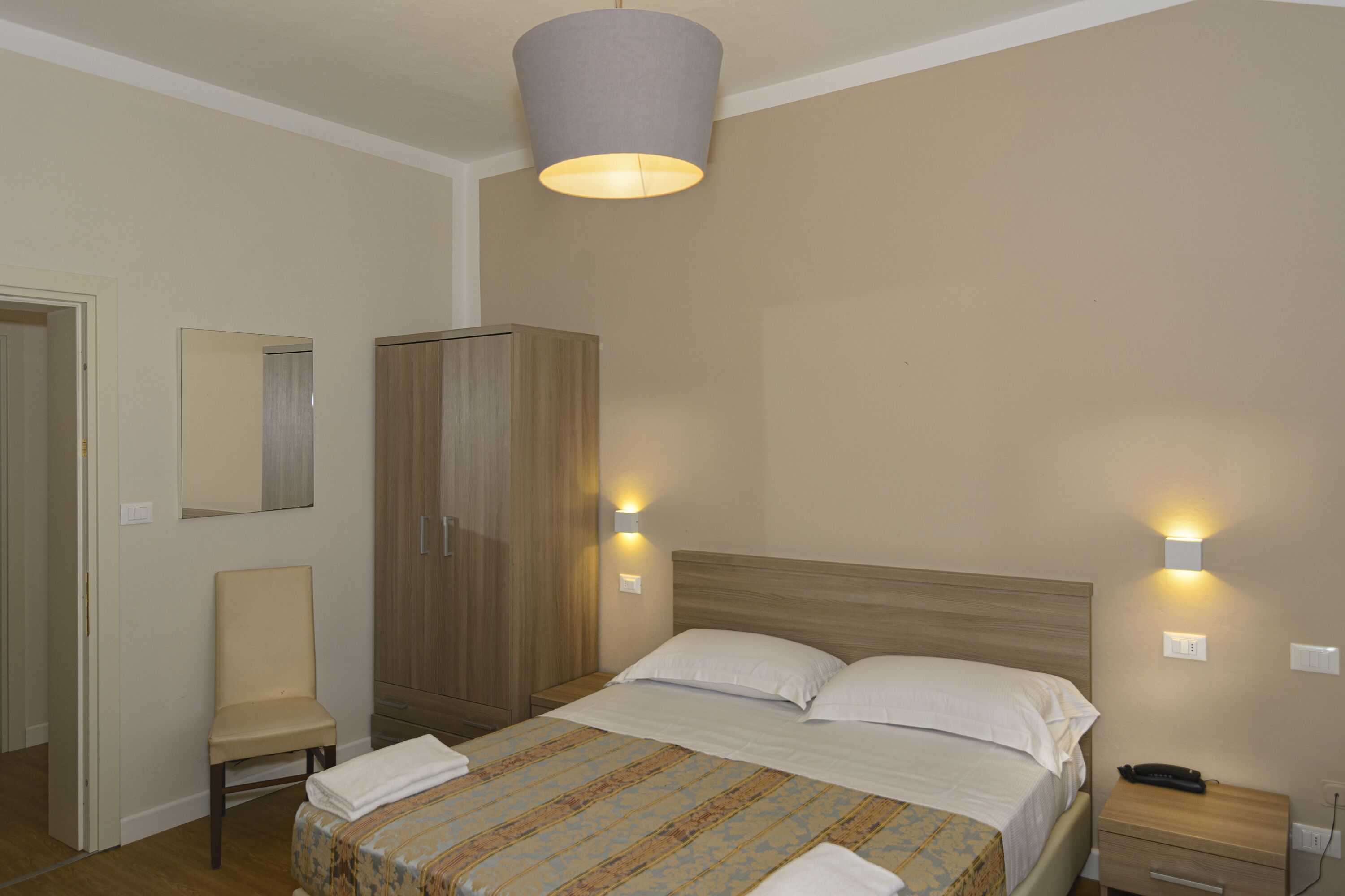 Una habitación de hotel con una cama, una silla, un armario y dos luces fijadas a la pared.