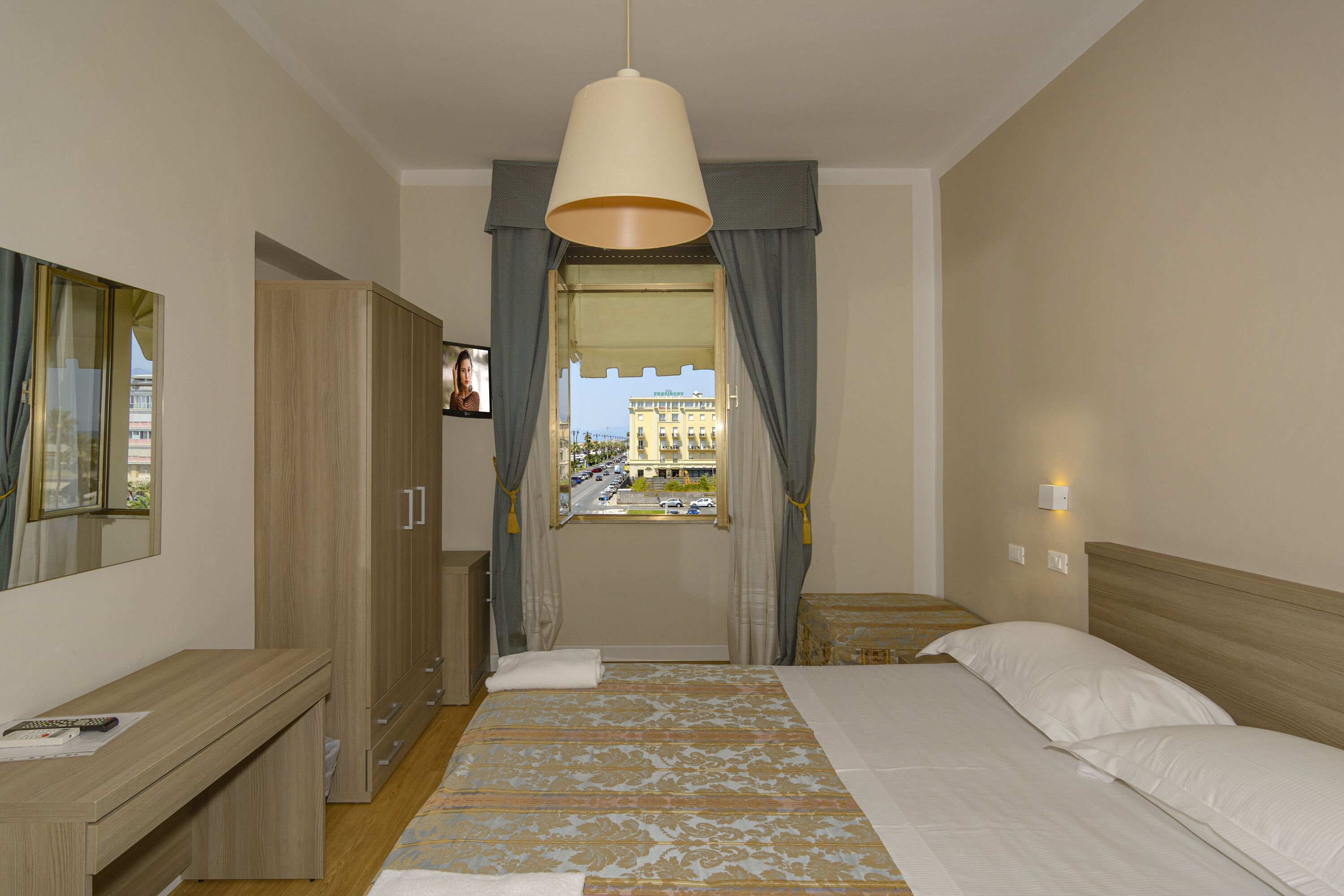 Una camera d'albergo con un letto, un comodino, un armadio, una finestra con tende e vista all'esterno.