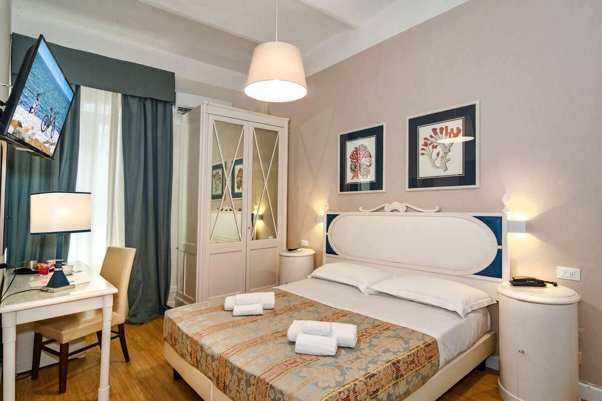 Ein Hotelzimmer mit Bett, Schreibtisch, Stuhl, Fernseher und Bildern an den Wänden.